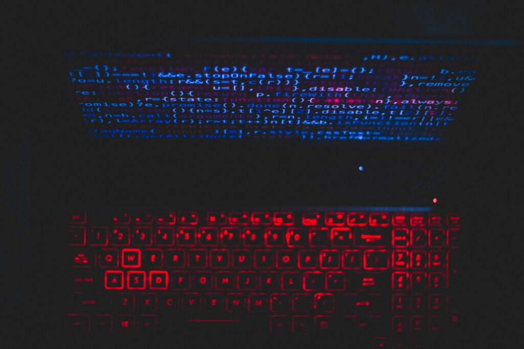 Dark-themed laptop with glowing red keyboard and code on screen, evoking adversarial manipulation of detection systems